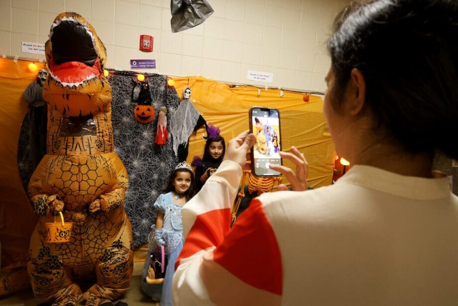 A parent takes a photo of her daughters next to an inflatable dinosaur Oct. 29, 2024, at Edward Stone Middle School during the Haunted Halls event.