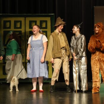 Dorothy, Scarecrow, Tinman, the Cowardly Lion, and a guard sing on stage during the high school musical production of 