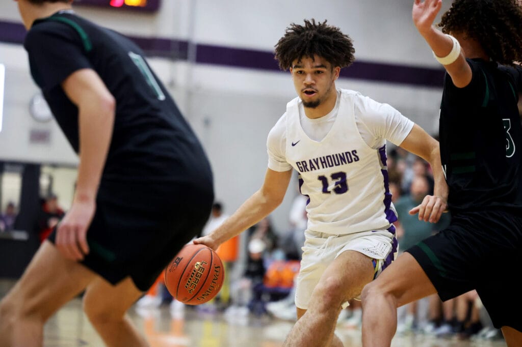 A member of the boys basketball team dribbles down the court between two players from the opposing team.