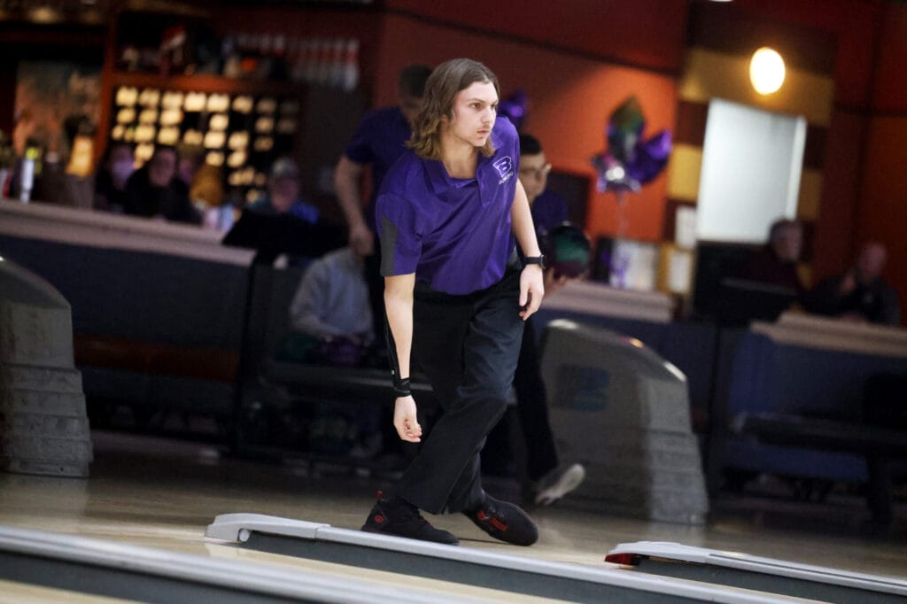 A member of the boys bowling team pauses to watch his ball roll down the lane.