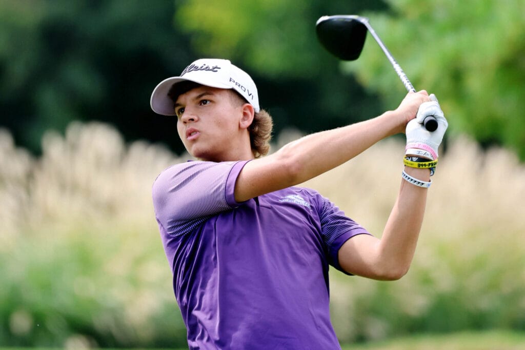 A member of the boys golf team holds a club behind his head while keeping an eye on the ball he just hit.
