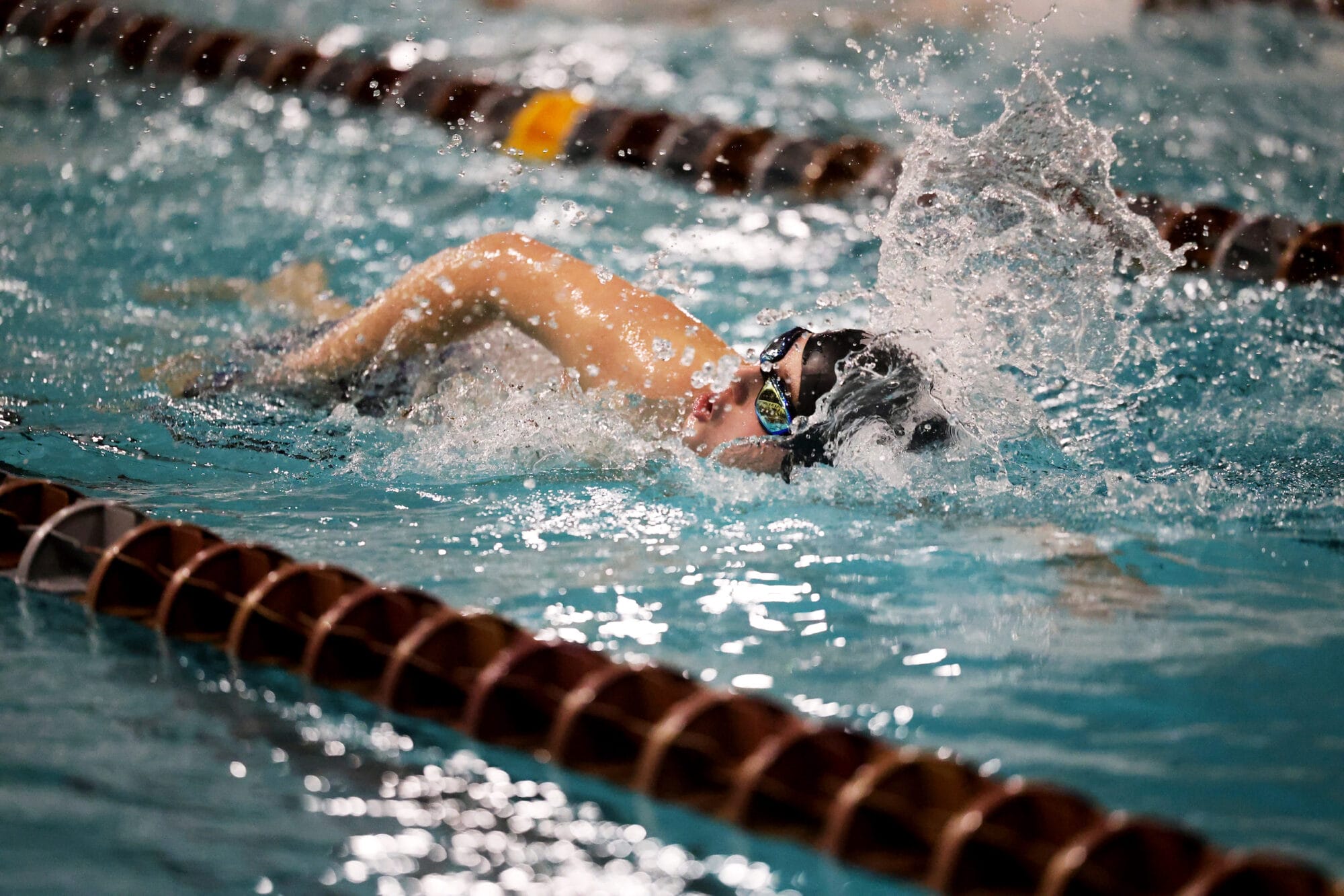 Water splashes up from the pool as a member of the boys swimming team swims toward the finish line.