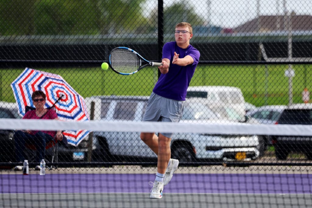 A member of the boys tennis team uses a racket to whack the ball back to his opponent.