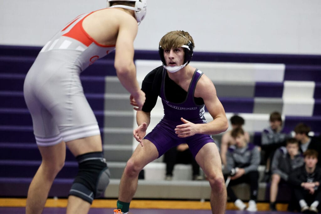A member of the boys wrestling team squats while facing his opponent.