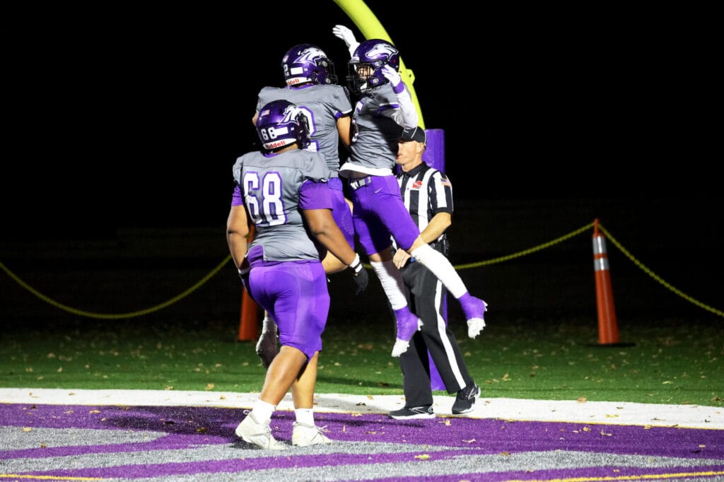 Two members of the football team jump in the air after a touchdown is scored while a third approaches to join in the celebration.