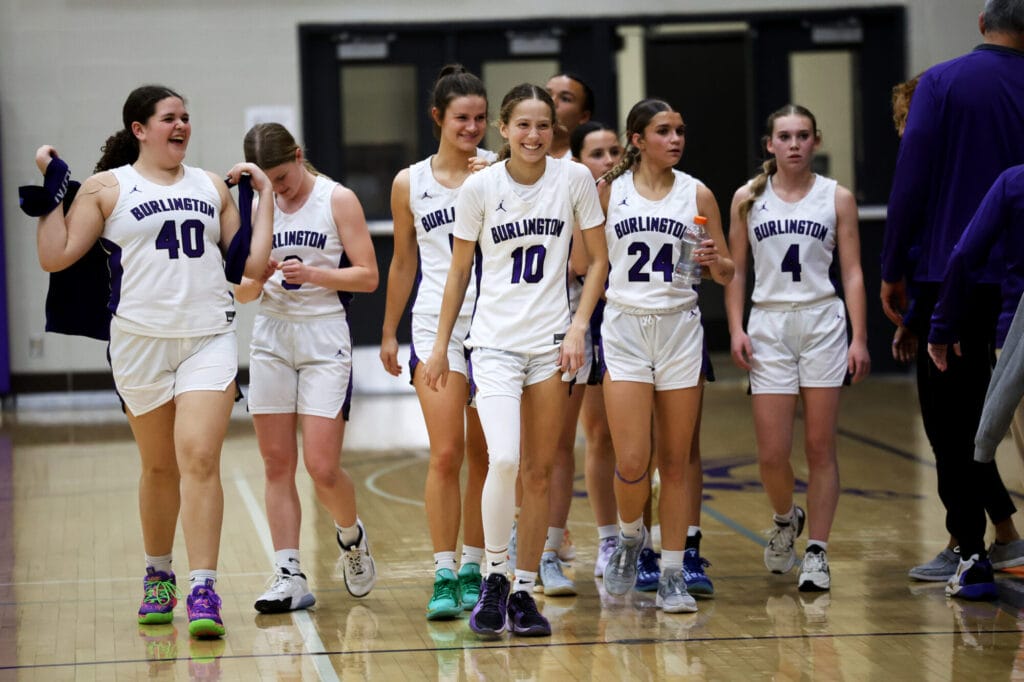 Members of the girls basketball team smile after winning their game while walking down the court.