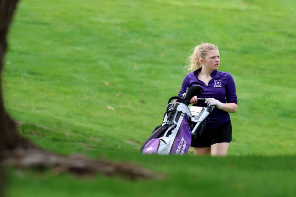 A member of the girls golf team looks on while moving her clubs to her ball.