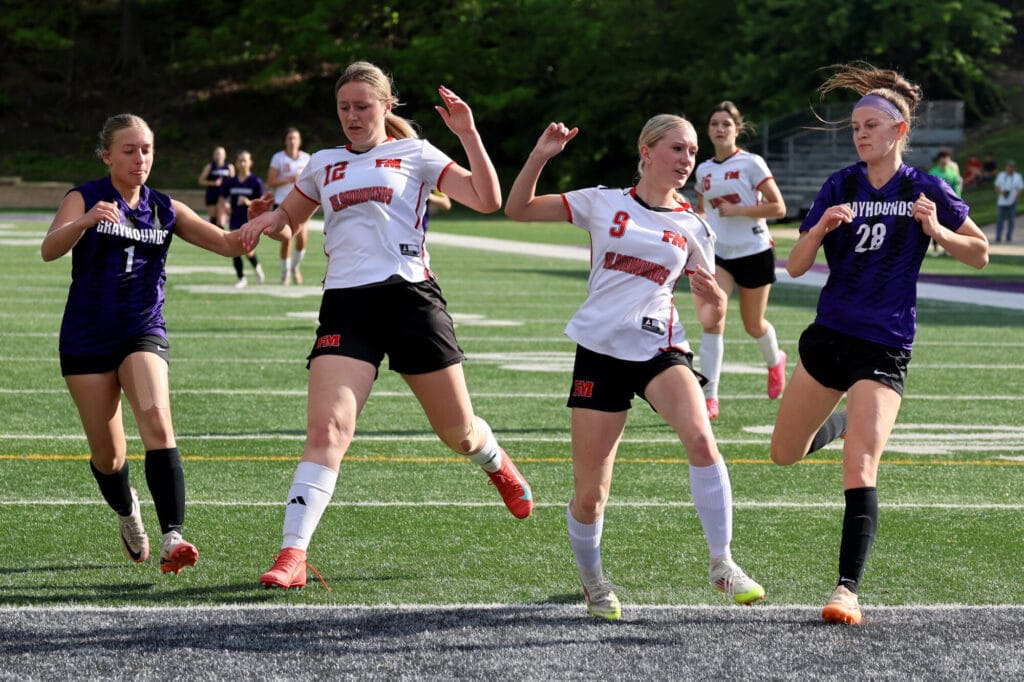 Two members of the girls soccer team flank two members of the opposing team during an intense game.