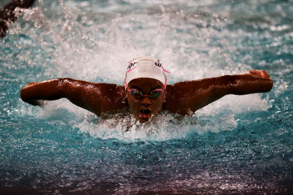 A member of the girls swimming and diving team emerges from the pool while doing the butterfly.