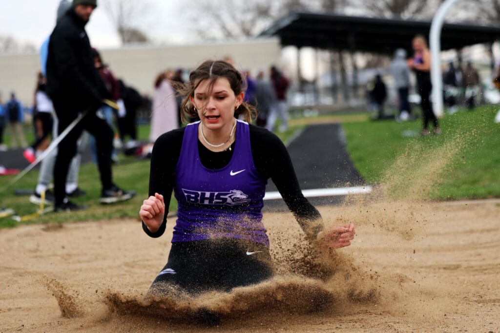 Sand flies into the air surrounding a member of the girls Track & Field team after she lands in the long jump pit.
