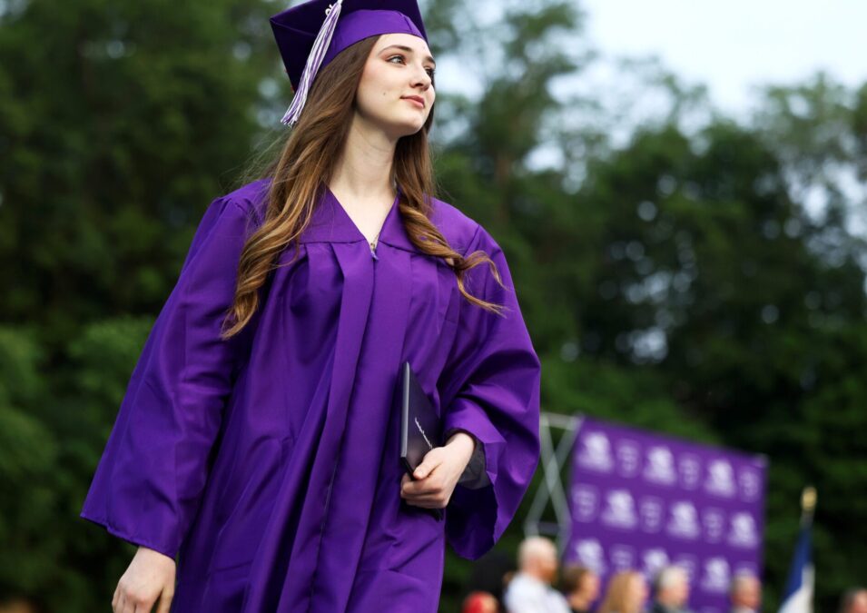 A young woman holds her head high while carrying her diploma cover after crossing the stage at her high school graduation.