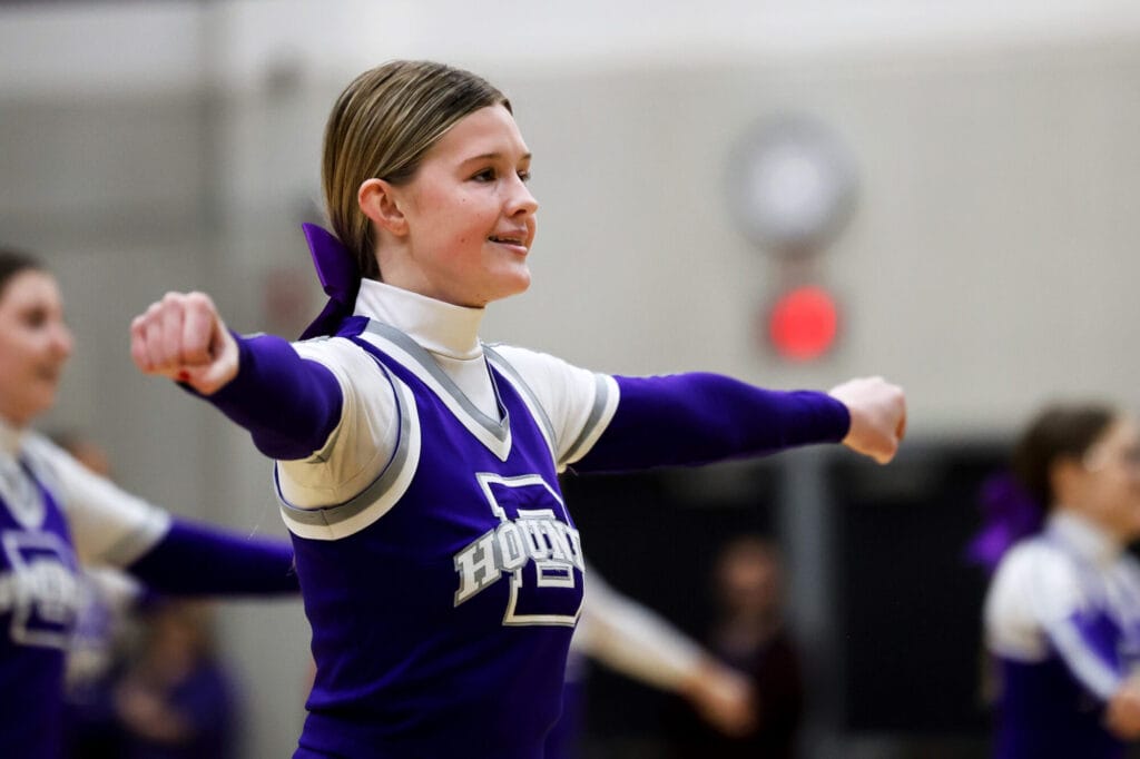 A cheerleader smiles while her arms are outstretched in a cheer.